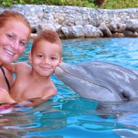 Een moeder en haar zoon in de zee, krijgen een kus van een dolfijn.